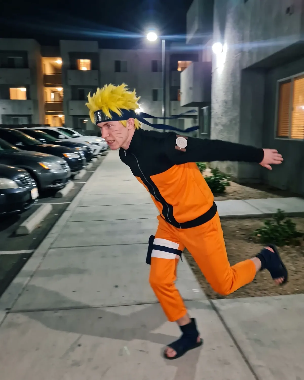 Naruto IRL sprinting past parked cars at night, arms stretched back, headband flying