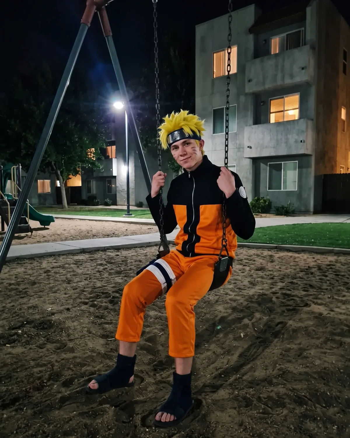 Naruto IRL alone on a playground swing at night under a streetlight